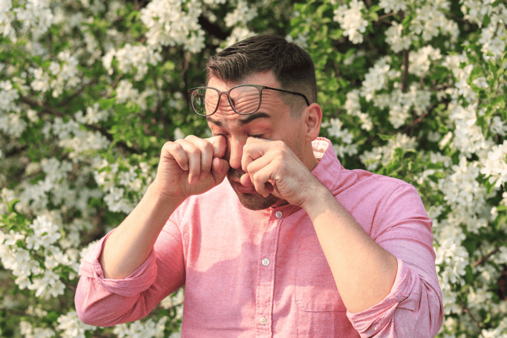 Man rubbing his eyes while standing by flowering bush