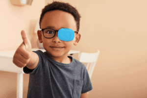 Young boy wearing glasses with an eye patch giving a thumbs up