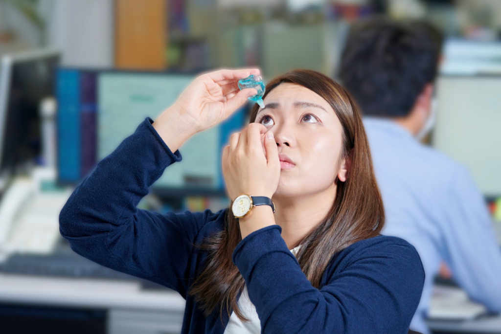 Woman putting in eye drops at work