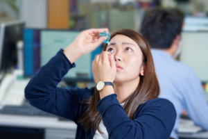 Woman putting in eye drops at work
