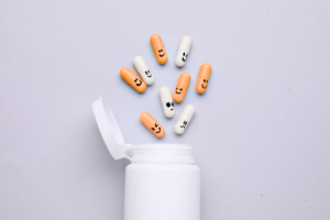 Medication bottle with orange pills with hand-drawn faces spilling out