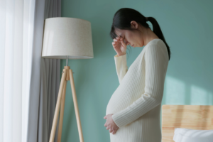 Pregnant woman standing up with her hand over her eyes, like she has a headache